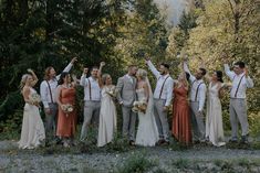 a group of people standing next to each other in front of trees with their arms up