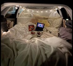 an open car trunk filled with lots of white sheets and blankets, two laptops on top of the bed