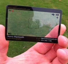 a person holding up a small card in front of a grassy area with trees and grass