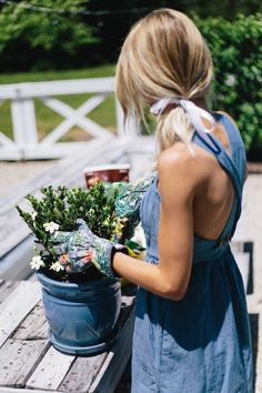 a woman in a blue dress holding a potted plant on a wooden picnic table