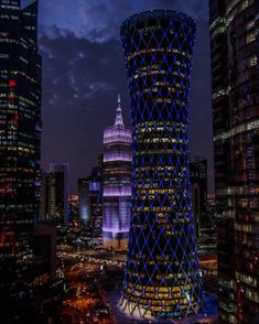 the tall building is lit up in blue and white lights at night, with other skyscrapers behind it