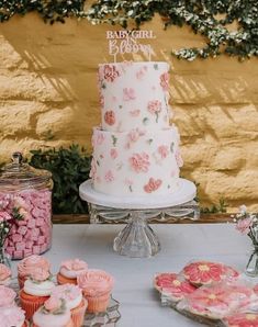 there is a cake and cupcakes on the table with pink flowers around it