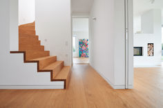 a wooden staircase leading up to a bright white room with wood flooring and artwork on the walls