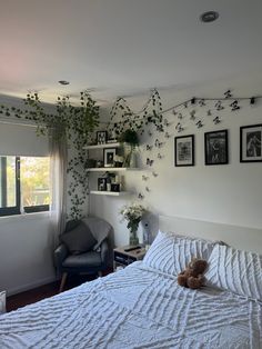 a bedroom with white walls and pictures on the wall above the bed, along with a teddy bear