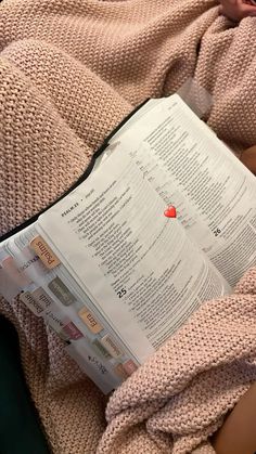 an open book laying on top of a bed next to a persons arm and leg