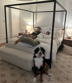 two people and a dog laying on a bed in a room with carpeted floors