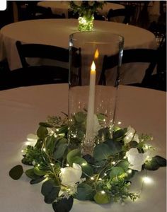 a candle that is sitting on top of a table with flowers and greenery around it