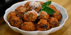 a white bowl filled with meatballs covered in parmesan cheese and garnish