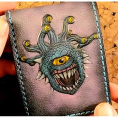 a hand holding up a wallet with an image of a monster on it's face