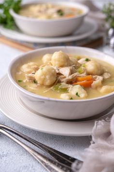 a bowl of soup with dumplings and carrots on a plate next to silverware