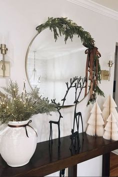 a table topped with a white vase filled with greenery next to a round mirror