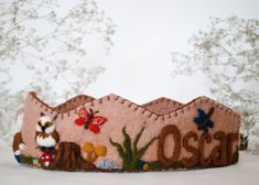 a pink felt crown with an owl and other animals on it, sitting in front of a white background