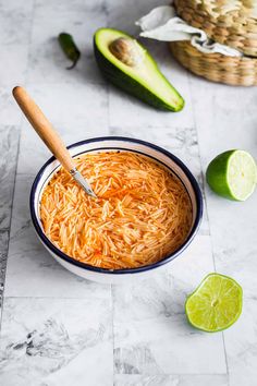 a bowl filled with shredded cheese next to limes and an avocado on the side