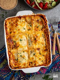 a casserole dish with meat and vegetables in it next to a bowl of salad