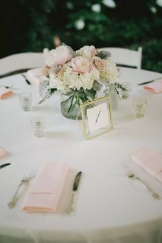 the table is set with pink napkins, silverware and flowers in a vase