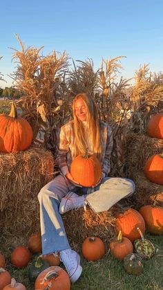 a woman sitting on top of hay bales with pumpkins in front of her