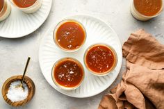 four sauces on plates with spoons next to them and salt in small bowls