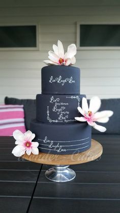 a three tiered cake with white flowers on the top and writing on the bottom