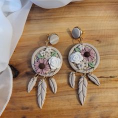 two pairs of earrings with flowers and feathers hanging from them on a wooden table top