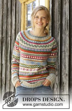 a woman standing in front of a wooden door wearing a colorful sweater and smiling at the camera