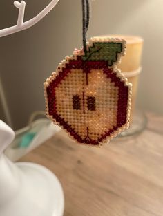 a cross stitch ornament hanging from a string on a table next to a candle