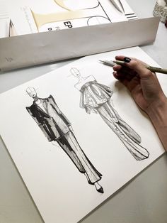 a woman's hand is holding a pen and sketching the design for a dress