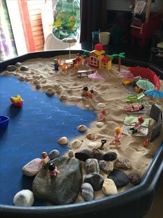 there are many toys in the sand on this beach play table with water and rocks