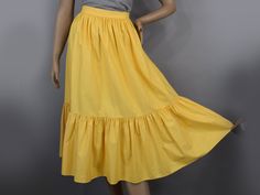 This sunny yellow vintage 80s skirt will be a great starting point for your retro and western inspired outfits. The easy care cotton fabric is medium weight but still comfortable to wear. It has loads of tucks set at the waistband, which fall out to the knees, where a second tier is set with even more tucks that fall out to the hem. There is a loop detail at the lower seam on each side. Top it with a belt as shown (not included) for a great look.   Label Picture Me   Fabric Cotton   Closures Snap at the waist Nylon zipper Condition Very Good No holes, tears or stains. There is a gap at the top of the zipper, which shows if not covered by a belt, or by an untucked blouse. It has been freshly laundered.    Measurements The measurements are as follows.  Measurements are of the garment, not th Retro Solid Color Skirt For Spring, Summer Retro Solid Color Skirt, Yellow Gathered Skirt Bottoms In Cotton, Vintage Cotton Bottoms With Ruffled Skirt, Retro Cotton Tiered Skirt, Yellow Cotton Bottoms With Ruffles, Retro Cotton Skirt With Ruffles, Yellow Tiered Skirt, Yellow Cotton Ruffled Bottoms