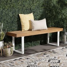 a wooden bench with two pillows on it next to a wall covered in greenery