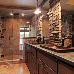 a bathroom with two sinks and a walk in shower next to a stone wall behind the sink