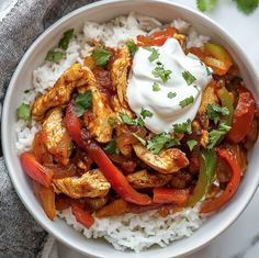 a white bowl filled with chicken and peppers covered in sour cream on top of rice