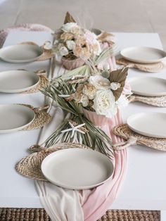 the table is set with white plates and flowers