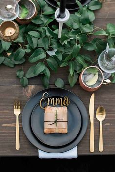 a black plate topped with a piece of cake next to utensils and greenery