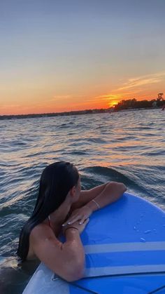 a woman sitting on top of a surfboard in the ocean at sunset or dawn