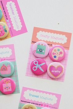 three different buttons on a white surface with pink and blue trimmings, some have scissors