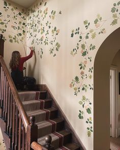 a woman is sitting on the stairs in front of a wall with leaves painted on it