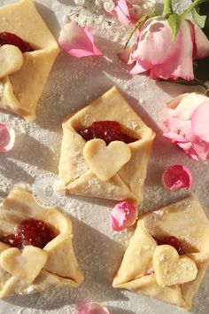 small pastries with jam in the middle and pink flowers around them on a table