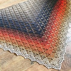 a multicolored crocheted shawl is laying on the floor next to a wooden table