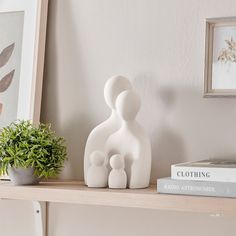 a couple of white sculptures sitting on top of a shelf next to a potted plant