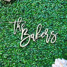 the baker's sign on top of a green wall with white flowers and greenery