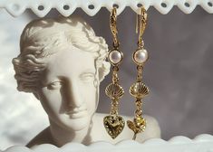 a pair of gold - plated earrings is displayed in a white display case with a statue behind it