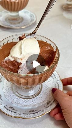 a person holding a spoon in a glass bowl filled with ice cream and chocolate pudding