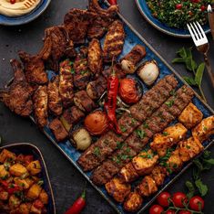 an assortment of meats and vegetables on a platter with utensils next to them