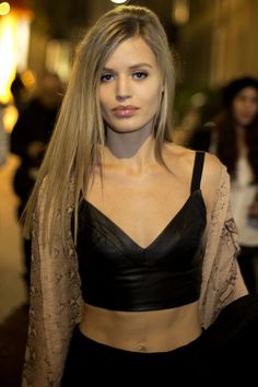 a woman with long blonde hair wearing a black bra top and leather pants, standing in front of a crowd