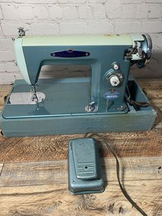 an old blue sewing machine sitting on top of a wooden table next to a brick wall