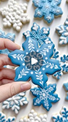 a hand holding a blue and white snowflake cookie in front of other decorated cookies