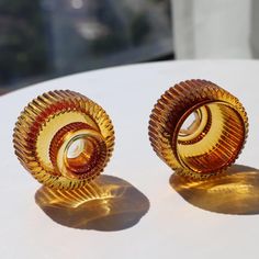 two gold colored earrings sitting on top of a white table next to an orange and yellow object