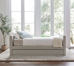 a white bed sitting on top of a wooden floor next to two windows with lots of windows