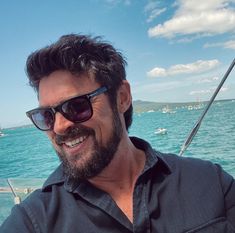 a man wearing sunglasses is sitting on a boat in the water and smiling at the camera