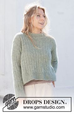 a woman standing in front of a white wall wearing a green sweater